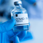A hand in latex glove holding COVID19 vaccine bottle